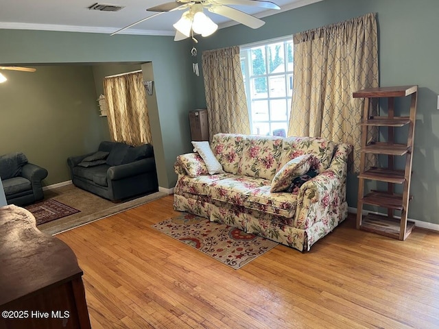 living room with wood finished floors, baseboards, a ceiling fan, visible vents, and ornamental molding