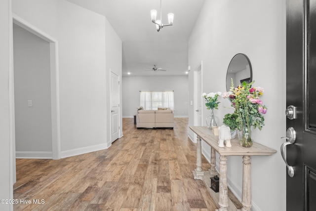 interior space featuring ceiling fan with notable chandelier, light wood-type flooring, and baseboards