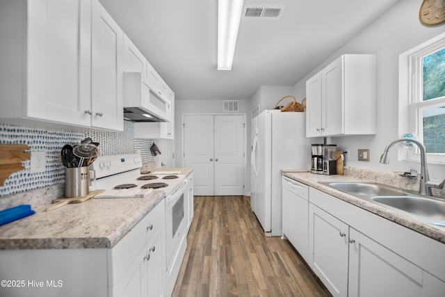 kitchen featuring a sink, visible vents, white appliances, and wood finished floors