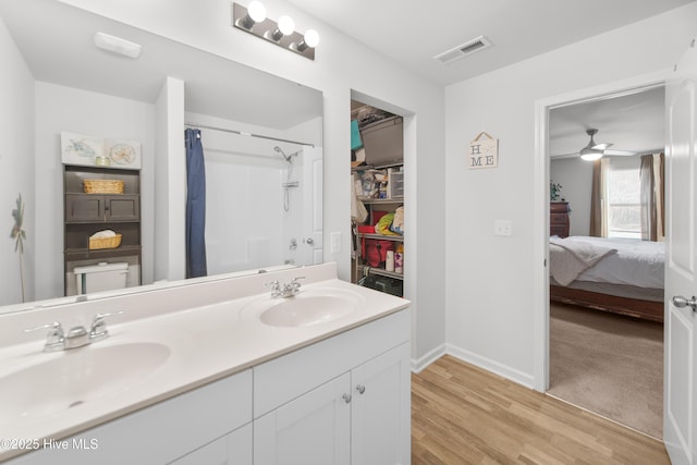 ensuite bathroom featuring a sink, visible vents, wood finished floors, and double vanity