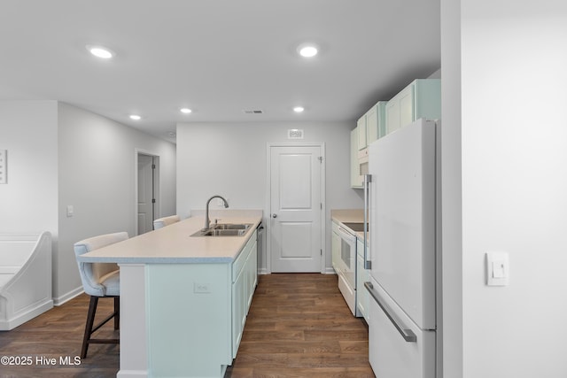 kitchen with dark wood-type flooring, light countertops, a kitchen bar, white appliances, and a sink