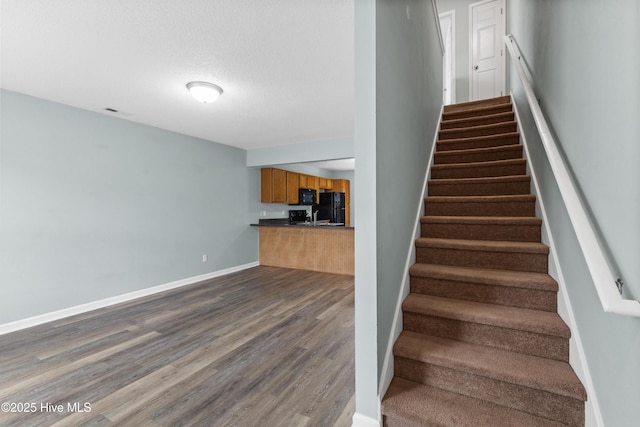 staircase featuring wood finished floors, baseboards, and a textured ceiling