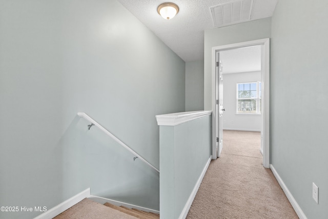 hall with an upstairs landing, visible vents, baseboards, and carpet