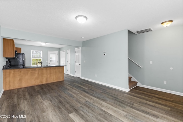 unfurnished living room featuring visible vents, baseboards, dark wood-type flooring, and stairs