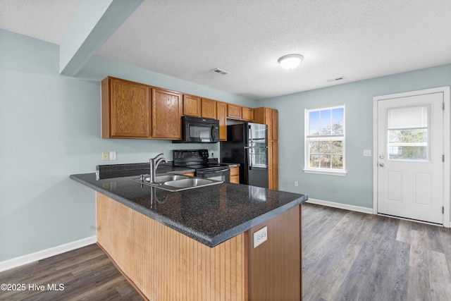 kitchen featuring dark wood-type flooring, brown cabinets, a peninsula, black appliances, and a sink