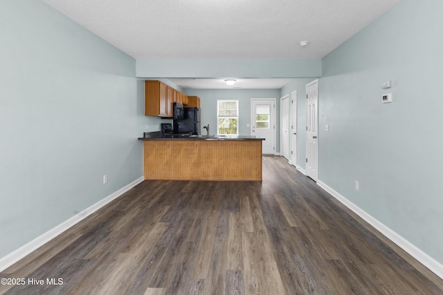 kitchen with dark countertops, baseboards, a peninsula, brown cabinetry, and black appliances