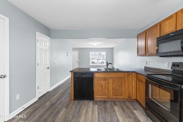 kitchen with a sink, dark countertops, black appliances, and a peninsula