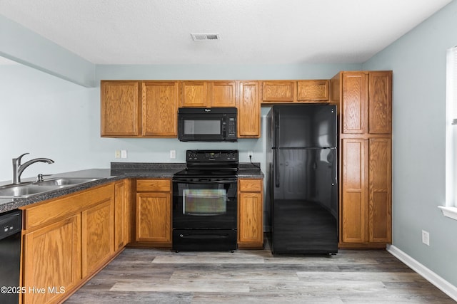 kitchen with a sink, visible vents, brown cabinets, and black appliances