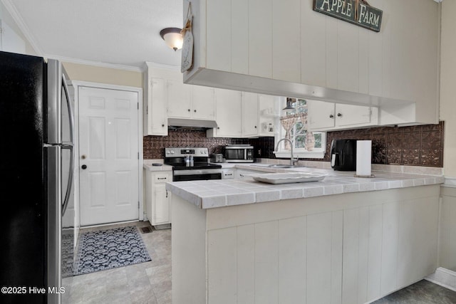 kitchen with crown molding, under cabinet range hood, a peninsula, stainless steel appliances, and a sink