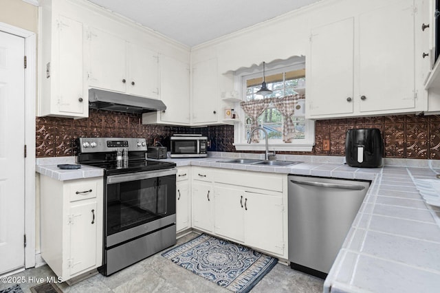 kitchen featuring under cabinet range hood, a sink, stainless steel appliances, white cabinets, and tile counters