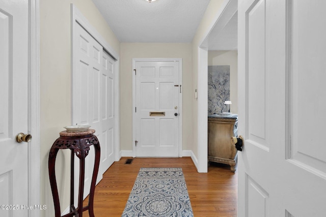 foyer entrance with light wood-type flooring, baseboards, a textured ceiling, and visible vents