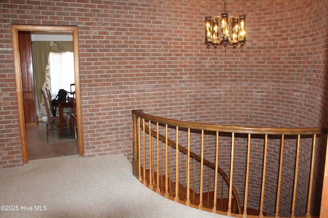 hall with an upstairs landing, a notable chandelier, brick wall, and carpet floors