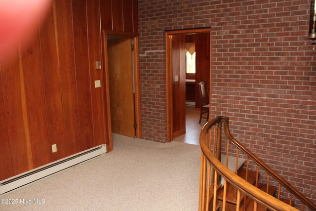 hall featuring carpet, brick wall, wood walls, a baseboard heating unit, and an upstairs landing