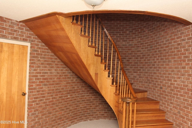 stairs featuring vaulted ceiling and brick wall