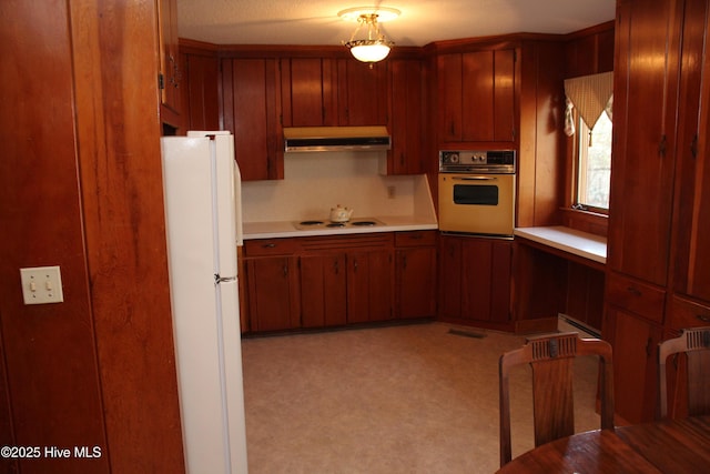 kitchen featuring white appliances, light countertops, brown cabinets, and under cabinet range hood