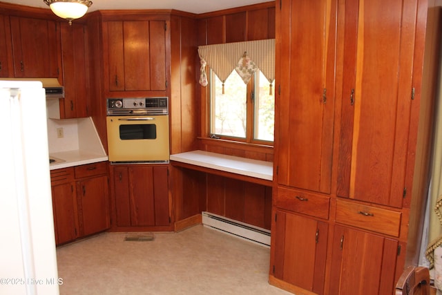 kitchen with wall oven, light countertops, brown cabinetry, built in study area, and a baseboard radiator