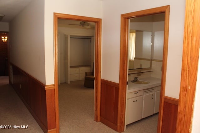 hallway with a sink, light carpet, wood walls, and wainscoting