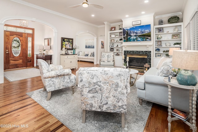 living room with ornamental molding, a ceiling fan, wood finished floors, arched walkways, and a fireplace