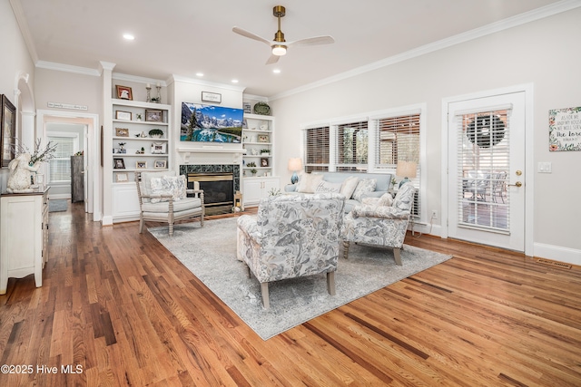 living room with a fireplace, crown molding, a ceiling fan, and wood finished floors