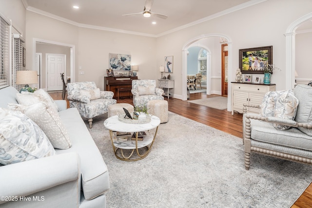 living area with ceiling fan, arched walkways, wood finished floors, and ornamental molding