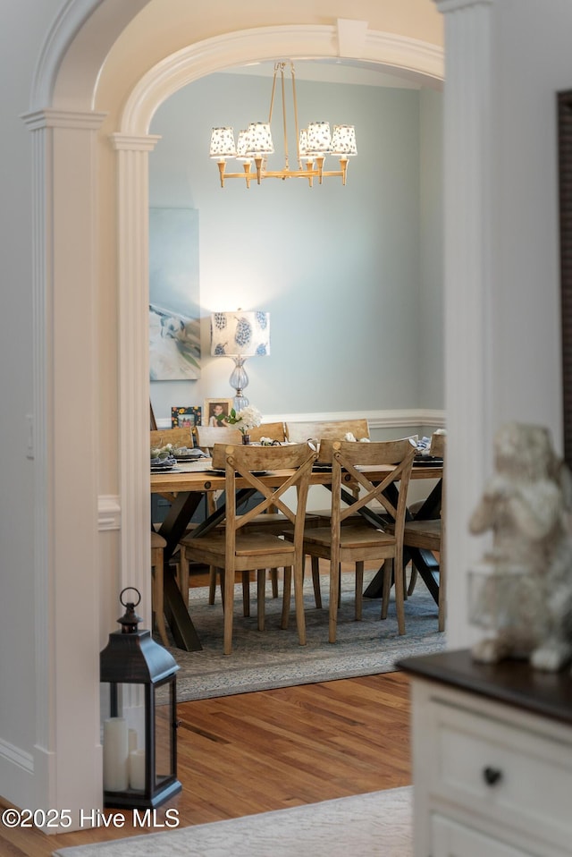 dining space featuring decorative columns, arched walkways, an inviting chandelier, and wood finished floors