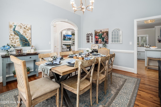 dining room with wood finished floors, baseboards, arched walkways, ornamental molding, and a notable chandelier