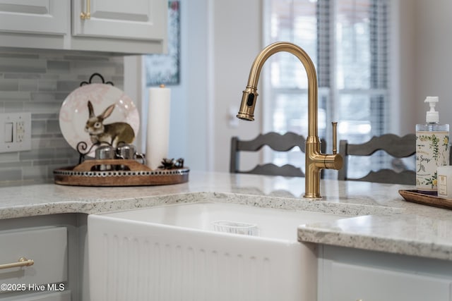 room details featuring decorative backsplash, white cabinets, light stone countertops, and a sink