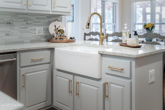 kitchen with a sink, backsplash, white cabinetry, light stone countertops, and dishwasher