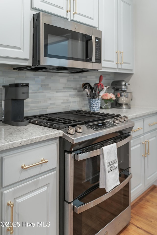 kitchen with decorative backsplash, white cabinets, appliances with stainless steel finishes, and light wood-style floors