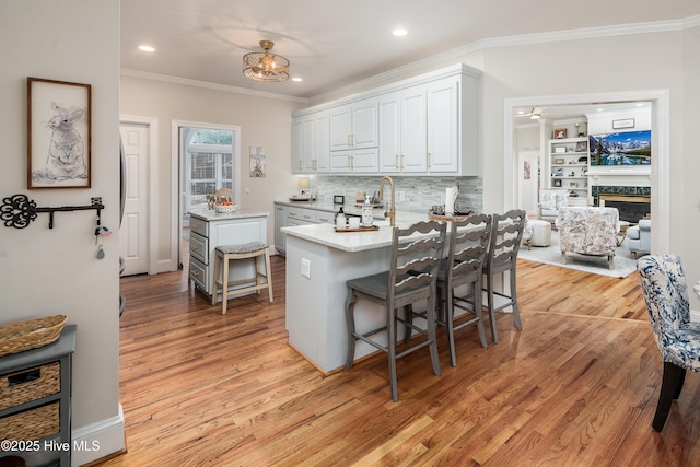 kitchen with crown molding, white cabinetry, light wood-type flooring, and a kitchen breakfast bar