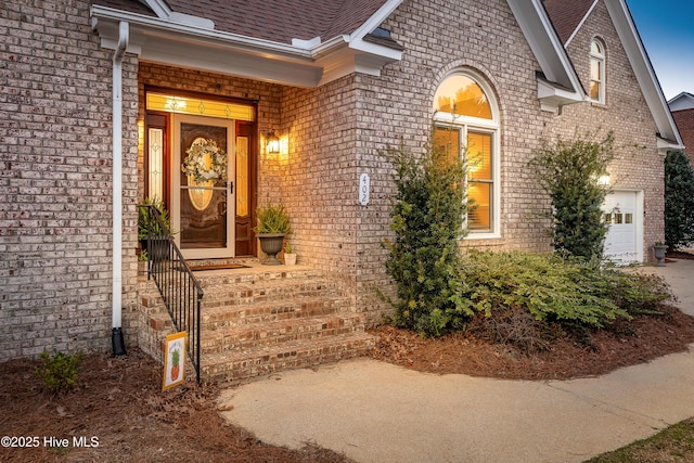 property entrance with brick siding, roof with shingles, and an attached garage