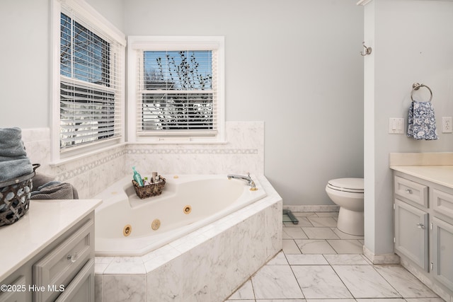 bathroom with a jetted tub, baseboards, toilet, marble finish floor, and vanity