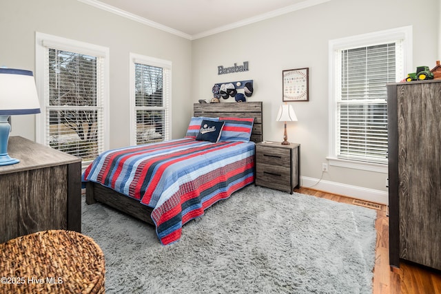 bedroom with visible vents, baseboards, wood finished floors, and crown molding