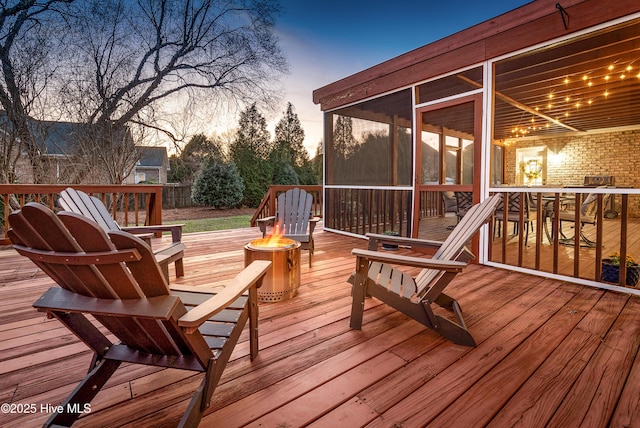 deck at dusk with an outdoor fire pit and a sunroom