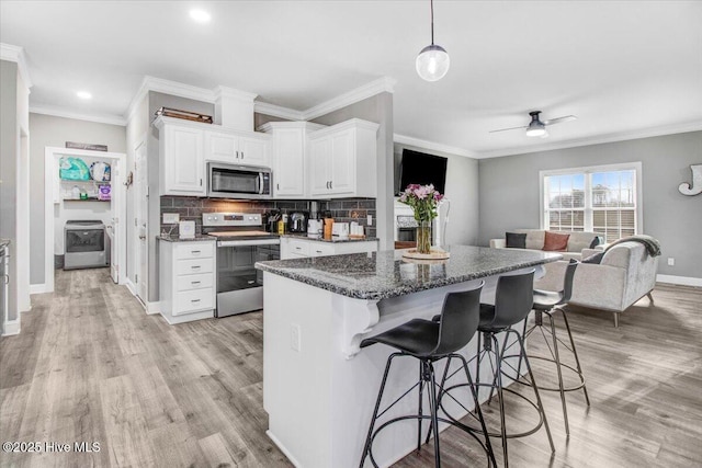 kitchen with light wood finished floors, a breakfast bar, ornamental molding, stainless steel appliances, and backsplash