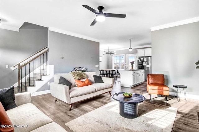 living area featuring stairway, a ceiling fan, baseboards, dark wood-style flooring, and ornamental molding