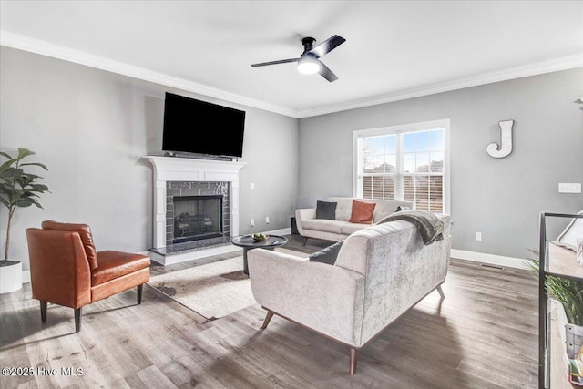 living room featuring ceiling fan, baseboards, ornamental molding, a tile fireplace, and wood finished floors