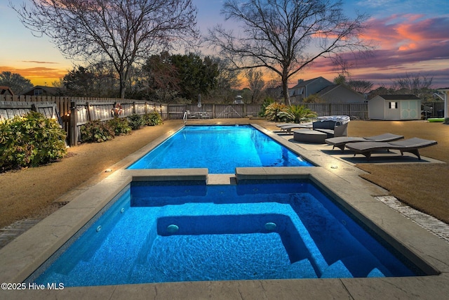 view of swimming pool featuring a pool with connected hot tub, a patio, a fenced backyard, a shed, and an outdoor structure