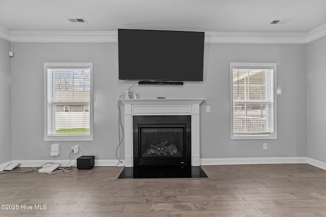 unfurnished living room with crown molding, a fireplace with flush hearth, wood finished floors, and visible vents