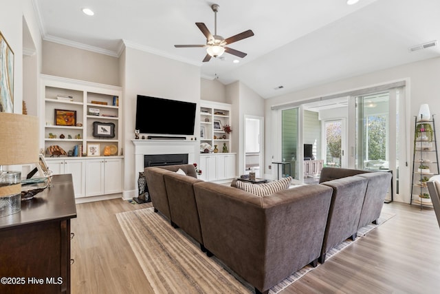 living room featuring visible vents, light wood-type flooring, lofted ceiling, ornamental molding, and a fireplace