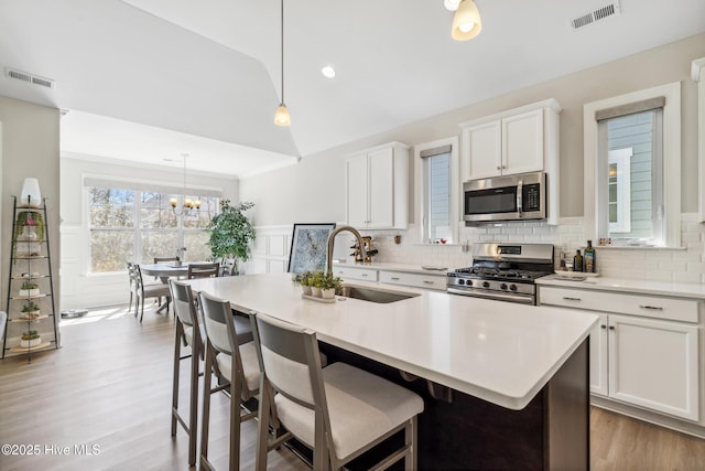 kitchen with a wainscoted wall, visible vents, lofted ceiling, a sink, and stainless steel appliances