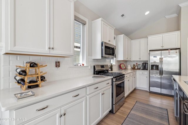 kitchen featuring light wood finished floors, lofted ceiling, decorative backsplash, appliances with stainless steel finishes, and white cabinetry