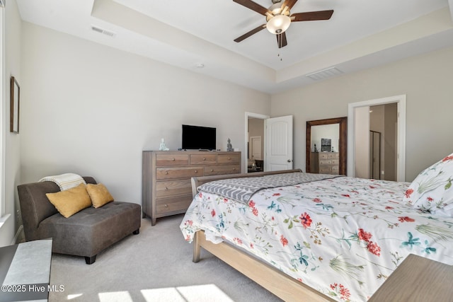 bedroom with a ceiling fan, a tray ceiling, light colored carpet, and visible vents