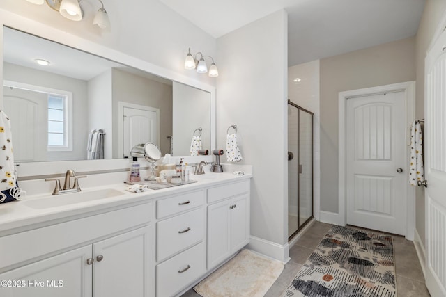 full bath featuring a sink, a shower stall, tile patterned flooring, double vanity, and baseboards