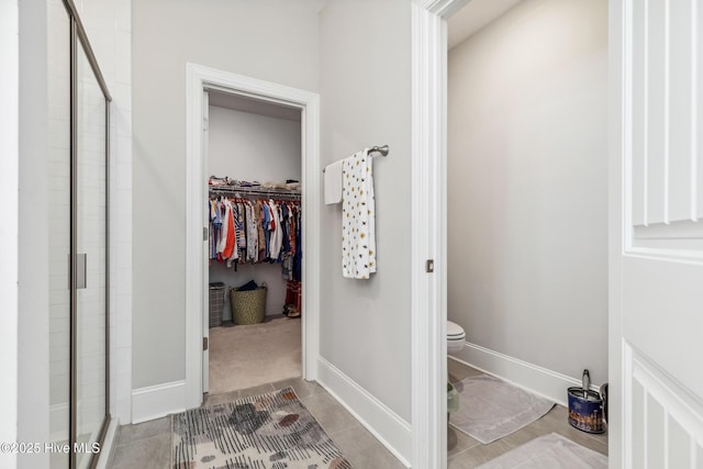 bathroom featuring a spacious closet, a stall shower, toilet, and baseboards