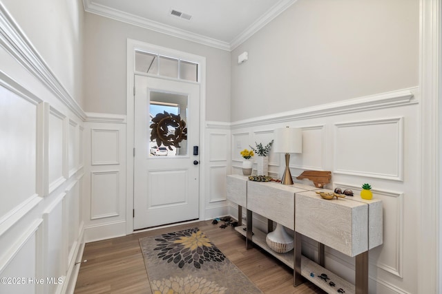 entryway featuring visible vents, ornamental molding, wood finished floors, wainscoting, and a decorative wall