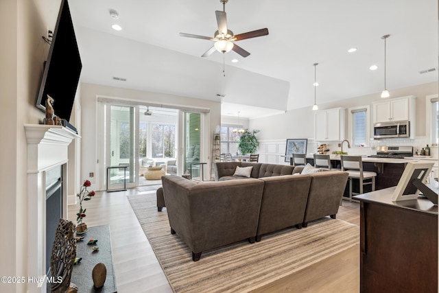 living area featuring light wood-style flooring, a fireplace, lofted ceiling, and ceiling fan