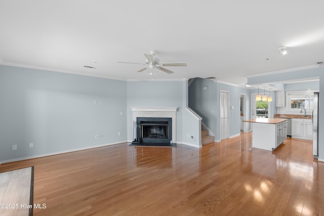 unfurnished living room featuring ceiling fan, light wood-style flooring, baseboards, a fireplace with flush hearth, and ornamental molding