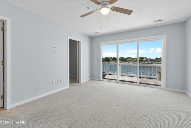 spare room with carpet flooring, a textured ceiling, a ceiling fan, baseboards, and visible vents