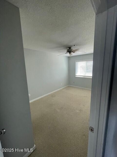 spare room featuring a textured ceiling, light carpet, baseboards, and ceiling fan